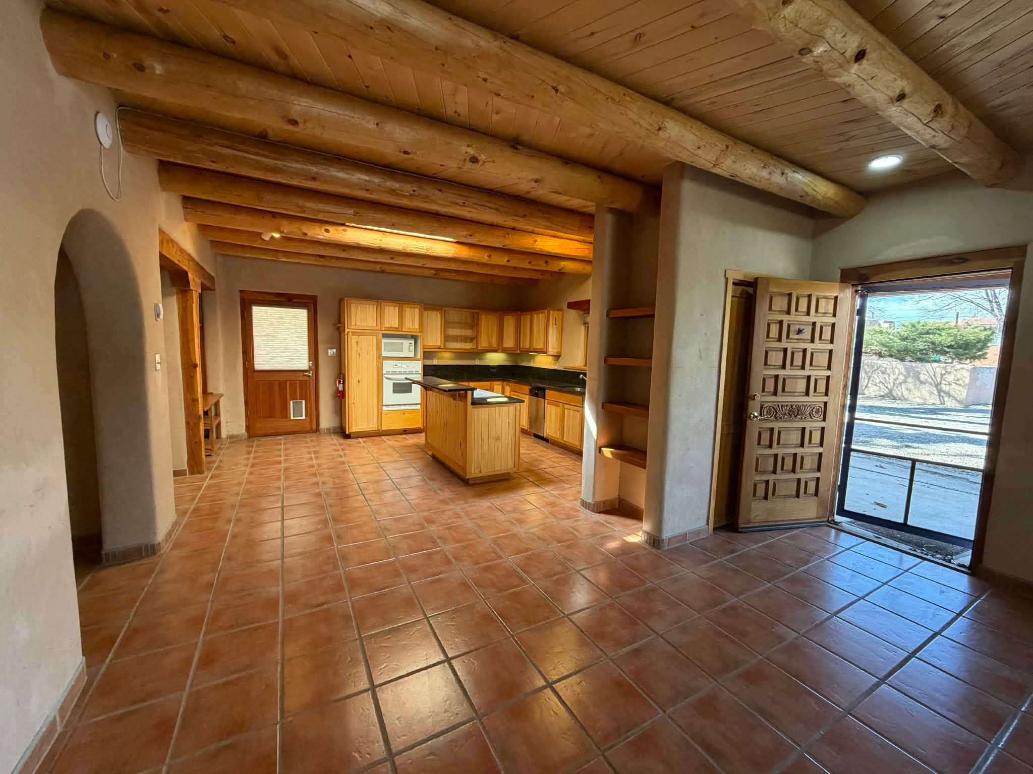 Spacious adobe kitchen with vigas ceiling, terracotta tile floors, and wood cabinetry